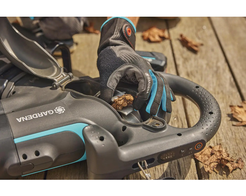 Aspirateur de feuilles sans fil Gardena avec clapet ouvert et main gantée en train d''enlever les feuilles
