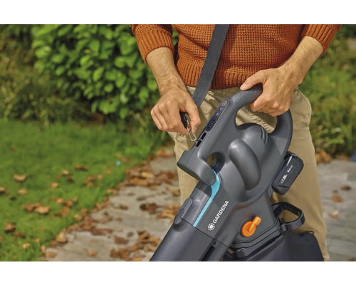 Une personne fixe un aspirateur souffleur de feuilles à batterie Gardena avec bandoulière