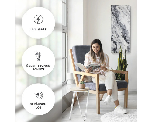 Une femme lit un magazine dans une pièce lumineuse et moderne avec un panneau chauffant au mur. Les symboles indiquent une puissance de 800 watts, une protection contre la surchauffe et un fonctionnement silencieux.