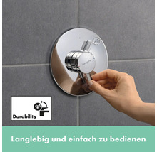 Nahaufnahme einer Hand, die einen runden, verchromten Hansgrohe Duschmischer an einer gefliesten Wand bedient. Das Symbol für Langlebigkeit ist ebenfalls im Bild zu sehen.