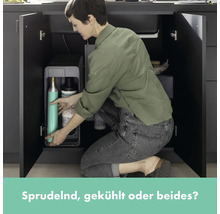 Frau befüllt Wassersprudler-System unter Spüle mit CO2-Zylinder