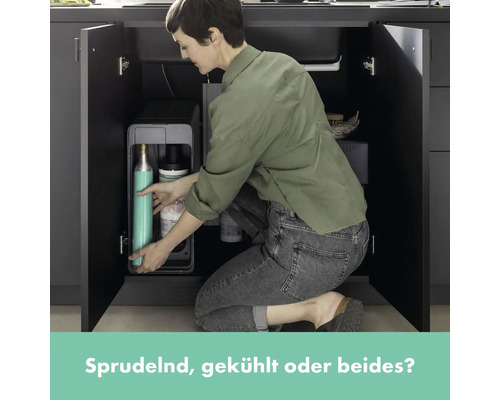 Frau befüllt Wassersprudler im Küchenschrank mit Zubehör.