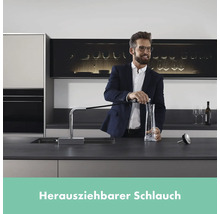 Mann füllt Wasser aus einer Küchenarmatur mit ausziehbarem Schlauch in eine Karaffe.