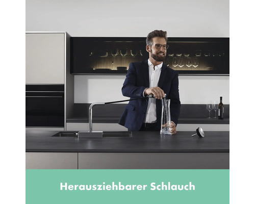 Mann füllt Wasser aus einer Küchenarmatur mit ausziehbarem Schlauch in eine Karaffe.