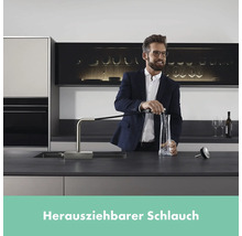 Mann füllt Wasser in eine Karaffe mit einer Spültischarmatur mit ausziehbarem Schlauch in einer modernen Küche.