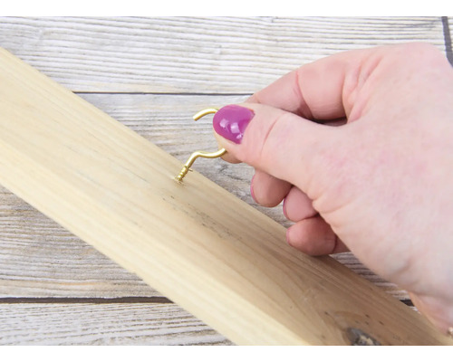 Une personne visse un crochet doré dans une planche en bois