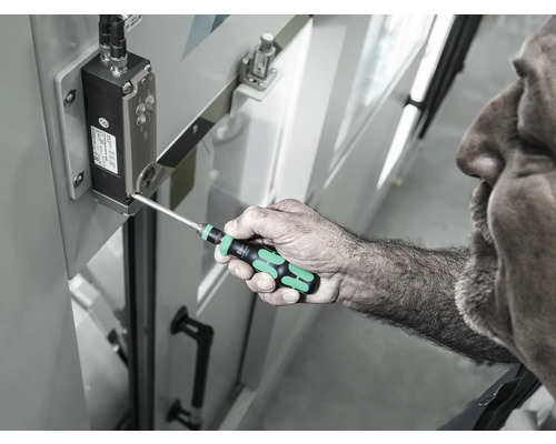 Ein Mann benutzt einen Schraubendreher, um eine Schraube an einem elektronischen Bauteil festzuziehen.