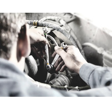 Un homme travaille sur un moteur avec deux clés plates.
