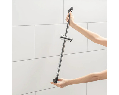 Eine Person hält eine Duschstange mit Duschkopfhalter vor einer gefliesten Wand.