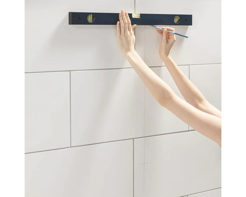 Eine Person verwendet eine Wasserwaage und einen Bleistift, um eine Linie auf Fliesen zu zeichnen.