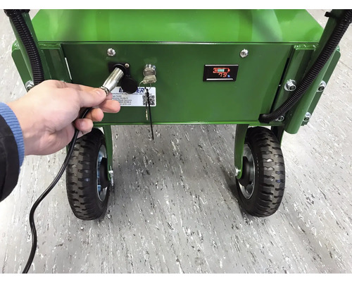Ein Mann schließt ein Ladegerät an eine grüne Schubkarre mit Batterieanzeige an