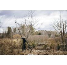 Une personne taille un arbre avec un ébrancheur dans le jardin.