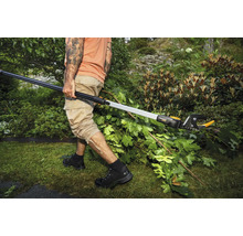 Une personne coupe des branches dans un jardin avec un sécateur télescopique.