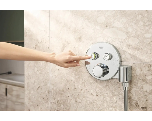 Eine Hand bedient eine Grohe Duscharmatur an einer gefliesten Wand.