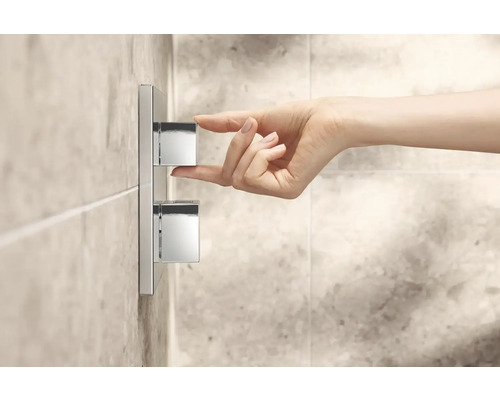 Une main actionne un mitigeur de douche en métal