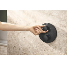 Main actionnant un thermostat de douche noir Grohe sur un mur carrelé