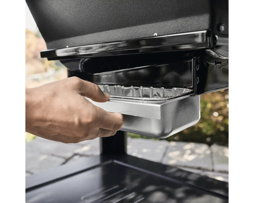 Une main tire le bac à graisse d''un barbecue.