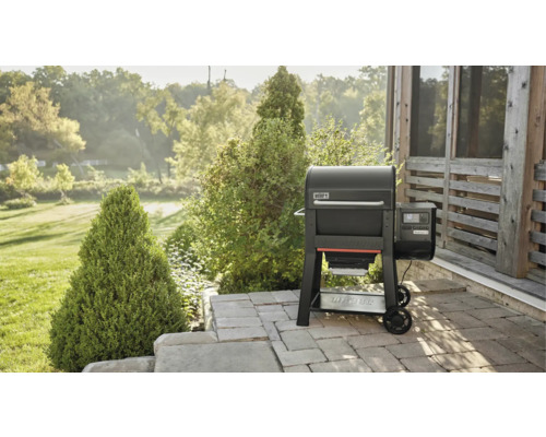 Grill à pellets Weber sur une terrasse avec un jardin en arrière-plan.