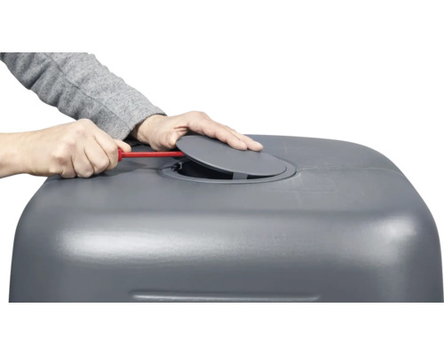 Personne manipule un tournevis sur une cuve à eau de pluie grise