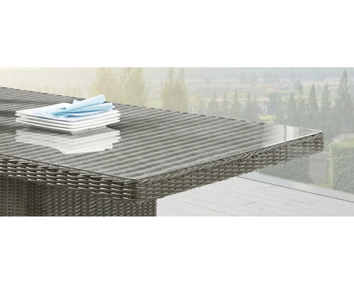 Detailansicht eines Gartentisches mit Glasplatte und Rattanoberfläche mit Geschirr