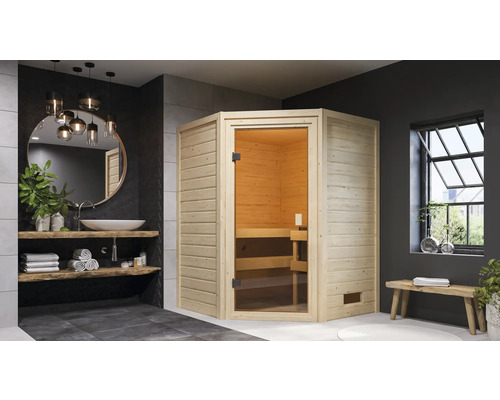 Sauna en bois clair avec porte en verre dans une salle de bains moderne avec lavabo, miroir et banc.