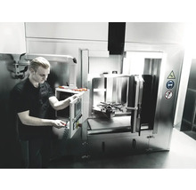 Un homme utilise une machine à laver industrielle avec des symboles d''avertissement pour la prudence, la protection des yeux et l''interdiction de fumer.