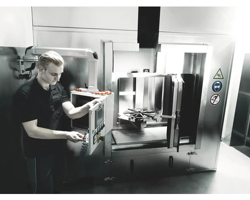 Un homme utilise une machine à laver industrielle avec des symboles d''avertissement pour la prudence, la protection des yeux et l''interdiction de fumer.