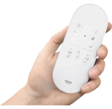 Une main tient une télécommande pour des toilettes de la marque Grohe.