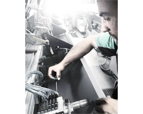 Un homme répare une machine avec un tournevis.