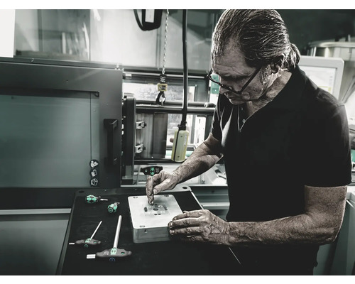 Ein Mann arbeitet an einem Werkstück mit Schraubendrehern in einer Werkstatt.