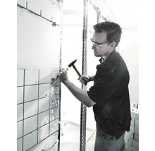 Un artisan portant des lunettes de protection retire des carreaux d''un mur à l''aide d''un marteau et d''un burin.