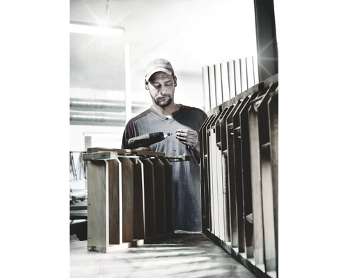 Artisan travaillant avec une perceuse sans fil sur un objet en bois dans un atelier.