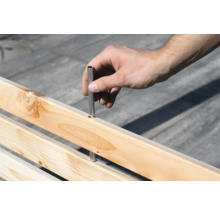 Hand setzt Metallstift in Holzkonstruktion ein