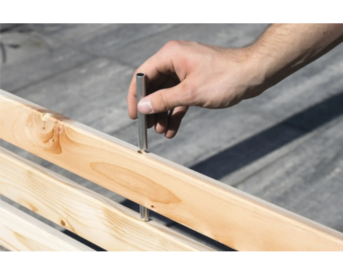 Hand setzt Metallstift in Holzkonstruktion ein