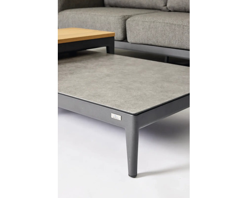 Vue détaillée d'une table de jardin avec un plateau en pierre et un cadre en métal, complétée par un canapé gris en arrière-plan