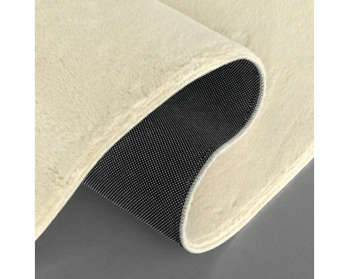 Detailansicht eines beigefarbenen Teppichs mit schwarzer, genoppter Rückseite.