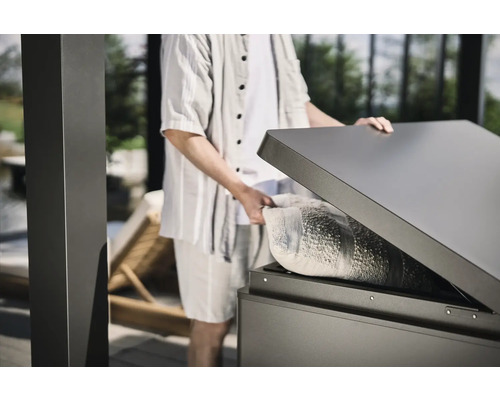 Person öffnet eine wetterfeste Aufbewahrungsbox im Außenbereich mit einem Kissen darin.