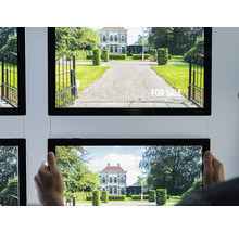 Plusieurs panneaux publicitaires immobiliers lumineux avec des images de maisons et de jardins sont accrochés à un mur