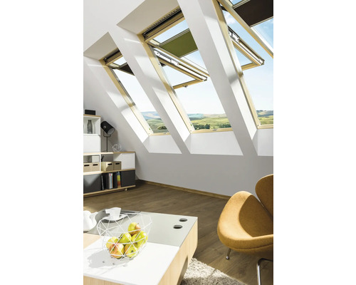 Chambre mansardée lumineuse avec plusieurs fenêtres de toit, partiellement ouvertes et équipées de protections solaires.