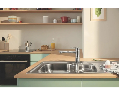 Küchenszene mit Spüle, Armatur und Küchenutensilien auf der Arbeitsfläche.