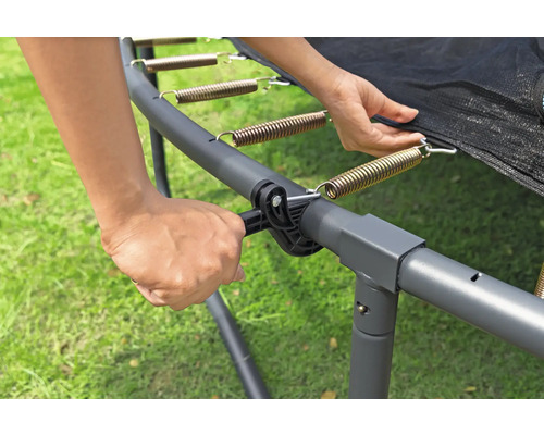 Une personne fixe un ressort au cadre du trampoline avec un tendeur