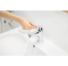 Eine Hand bedient einen glänzenden Wasserhahn an einem Waschbecken.