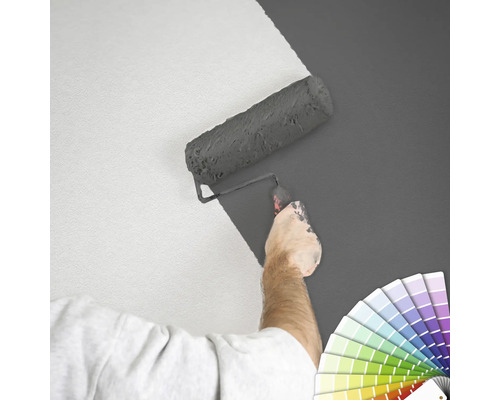 Eine Person streicht eine Wand mit einer Farbwalze und einer Farbpalette.