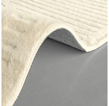 Vue détaillée d'un tapis de couleur claire avec une texture tissée et un coin retroussé montrant le dessous