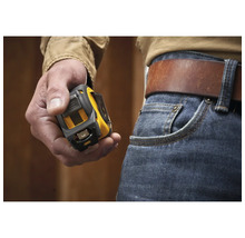 Une main tient un mètre ruban jaune et noir à côté d'un jean avec une ceinture