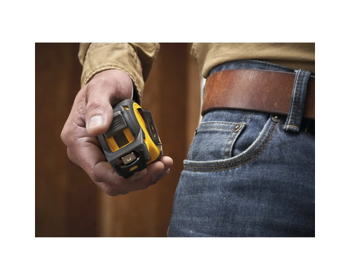 Une main tient un mètre ruban jaune et noir à côté d'un jean avec une ceinture