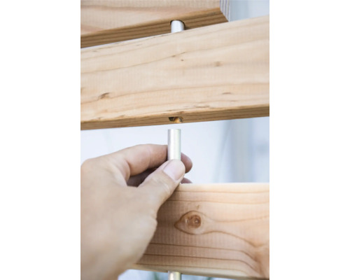 Detailansicht einer Holzkonstruktion mit silberfarbenen Metallstiften, die von einer Hand gehalten werden.