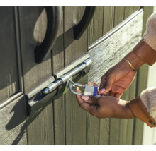 Eine Person sichert eine Tür mit einem Bolzenriegel und einem Vorhängeschloss.
