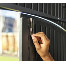 Eine Person betätigt einen Riegel an einer Gartentür zur Sicherung.