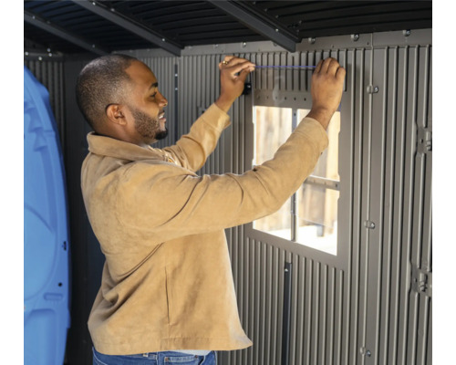 Ein Mann montiert ein Fenster in einem grauen Gartenhaus.